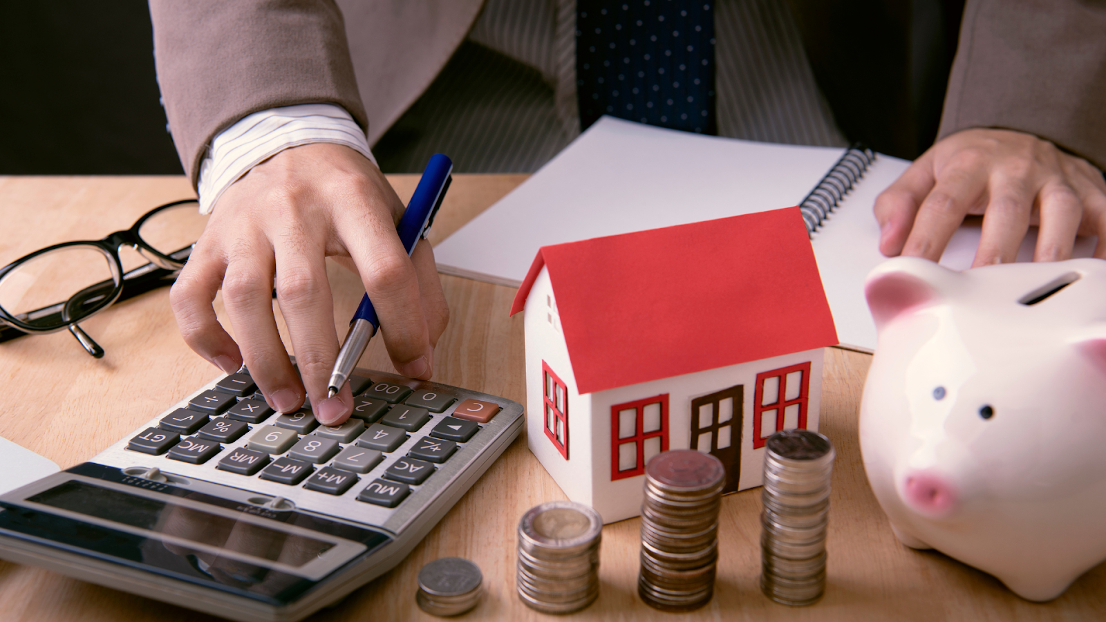 Calculating property tax beside a model home, coins, and piggy bank
