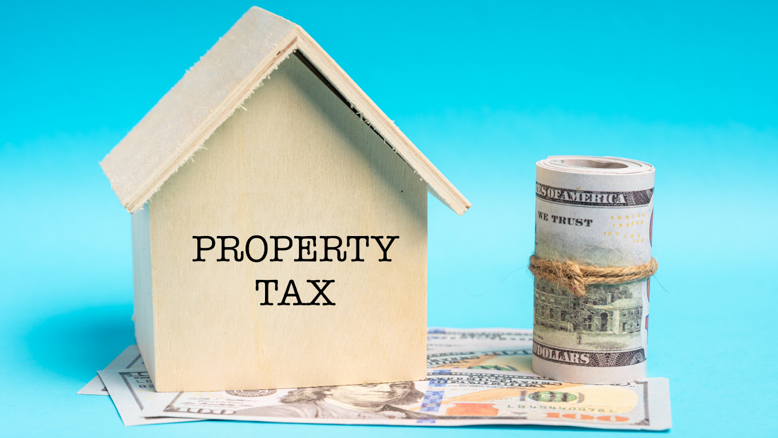 Property tax printed on mini wooden home with cash beside and underneath it