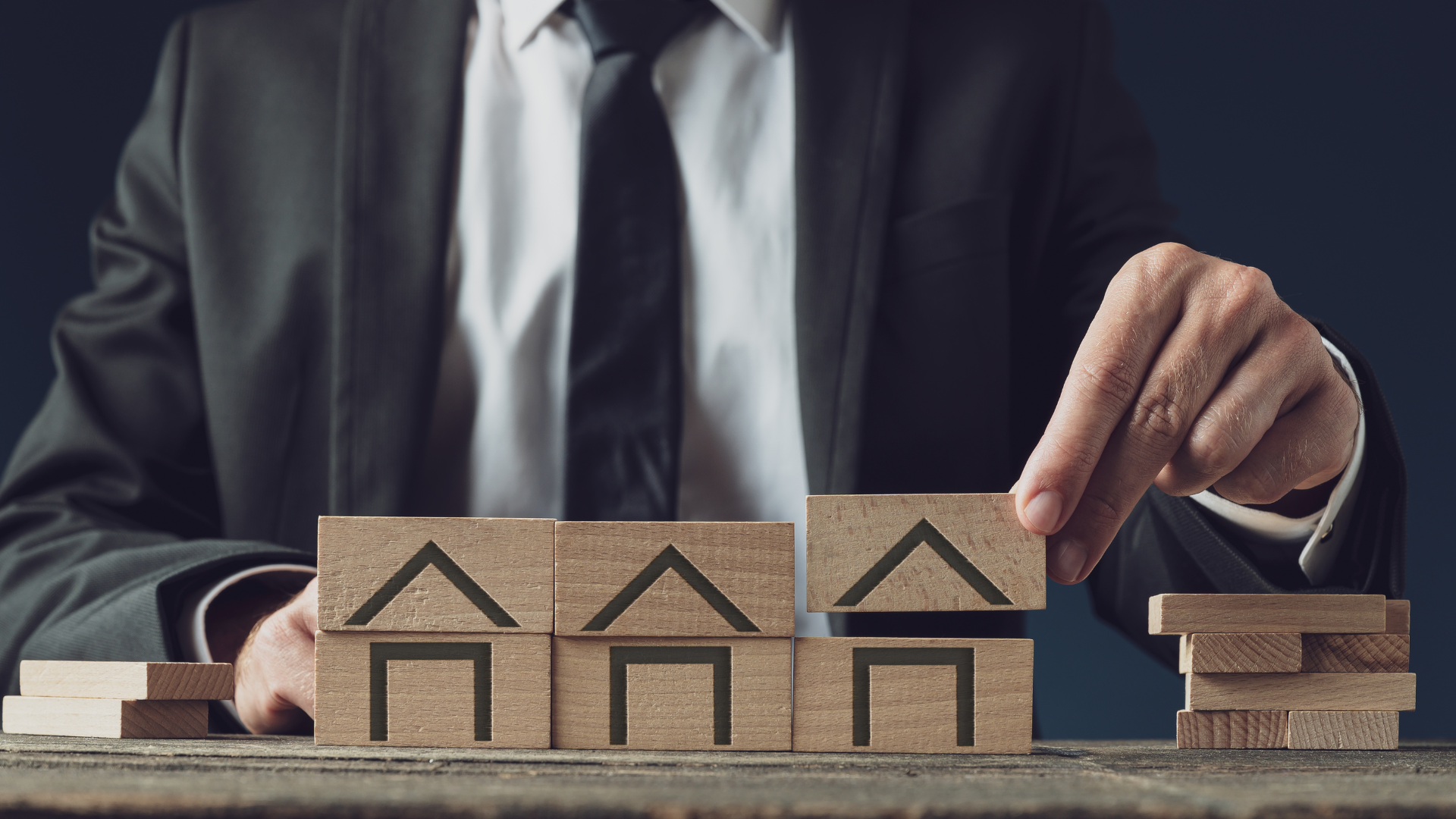 Professional arranging wooden house blocks representing property value assessment