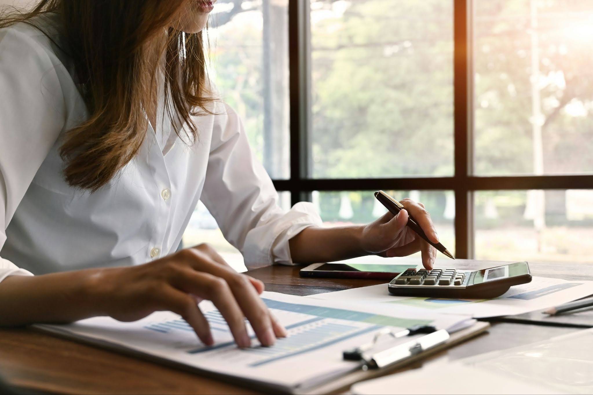 Woman reviewing financial documents and calculating property taxes with a calculator at a desk.